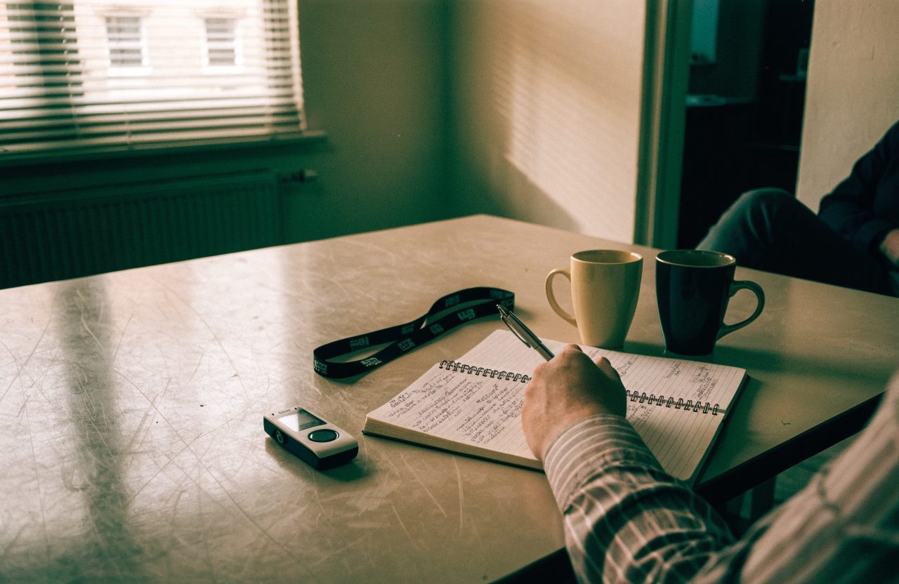 A voice recorder and a notebook of handwritten shorthand on a meeting-room table during an interview